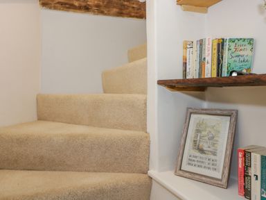 A carpeted staircase next to shelves with books and a framed quote at Fox Den Cottage in Castle Combe