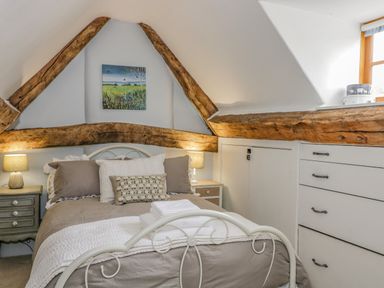A bedroom with a bed and bedside tables with lamps and exposed wooden beams at Fox Den Cottage in Castle Combe