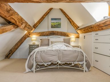 A bedroom with a metal bed frame under a pitched ceiling with exposed wooden beams and bedside tables with lamps at Fox Den Cottage in Castle Combe