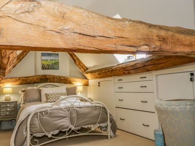 A bedroom with a bed a nightstand with lamps built in drawers and wooden beams at Fox Den Cottage in Castle Combe
