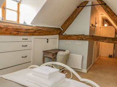 A bedroom with white towels on a bed a wooden desk and chair exposed wooden beams and a hallway at Fox Den Cottage in Castle Combe