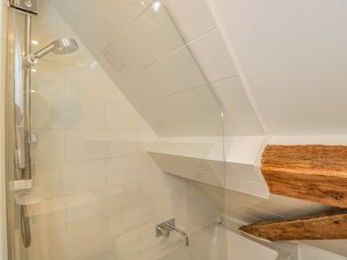 A shower area with a handheld showerhead and wooden beams at Fox Den Cottage in Castle Combe