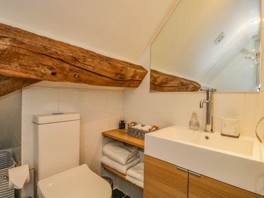A bathroom with a toilet sink wooden shelves towels and a large mirror at Fox Den Cottage in Castle Combe