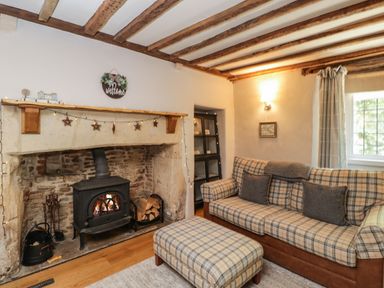 A living room with a wood stove fireplace and plaid sofa and ottoman at Fox Den Cottage in Castle Combe
