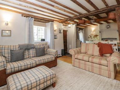 A living room with two patterned sofas a footstool and wooden ceiling beams at Fox Den Cottage in Castle Combe
