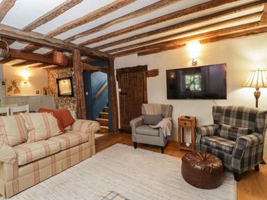 A living room with sofas armchairs a wall mounted TV and exposed wooden beams at Fox Den Cottage in Castle Combe