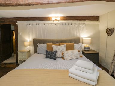 A bedroom with a double bed with pillows and folded towels on a blanket at Fox Den Cottage in Castle Combe