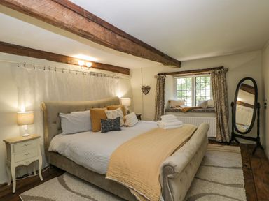 A bedroom with a large bed pillows bedside tables curtain a window seat and a standing mirror at Fox Den Cottage in Castle Combe