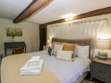 A bedroom with a bed with multiple pillows and folded towels on a yellow blanket a desk with a chair and a painting on the wall at Fox Den Cottage in Castle Combe