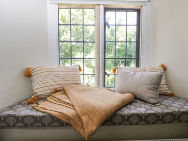A window seat with two striped pillows a plain pillow and a folded blanket at Fox Den Cottage in Castle Combe