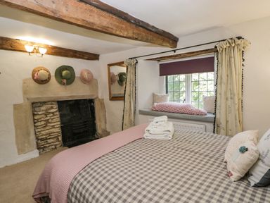 A bedroom with a bed near a window seat a fireplace and hats on the wall at Fox Den Cottage in Castle Combe