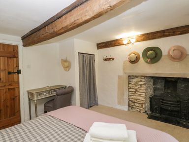 A bedroom with a checkered bedspread a wooden desk a chair hats on a wall above a fireplace at Fox Den Cottage in Castle Combe