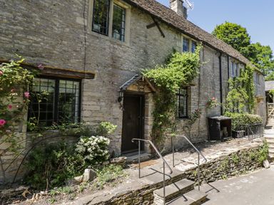 A stone cottage facade with climbing plants and flowers by the entrance steps at Fox Den Cottage in Castle Combe