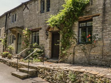 Stone exterior of a house with steps, metal handrails, windows, and plants at Fox Den Cottage in Castle Combe