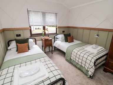 A bedroom with two single beds a wooden nightstand between them and a window with blinds at The Treeline in Swarland near Felton