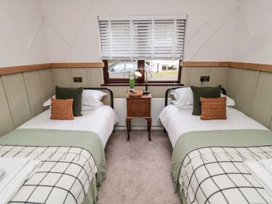 A bedroom with two single beds separated by a wooden nightstand under a window at The Treeline in Swarland near Felton