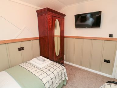 A bedroom with two single beds a wooden wardrobe with a mirror and a wall-mounted television at The Treeline in Swarland near Felton