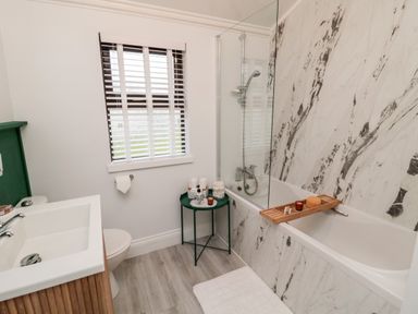 A bathroom with a bathtub a shower a white sink a toilet a small green table and a window with blinds at The Treeline in Swarland near Felton