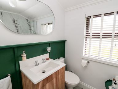 A bathroom with a sink vanity cabinet green wainscoting toilet and a window with blinds at The Treeline in Swarland near Felton