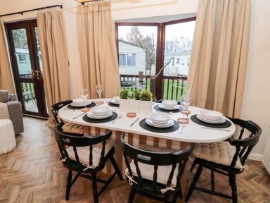 A dining area with a white table set for six black chairs with cushions and a bay window at The Treeline Swarland near Felton