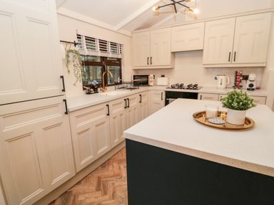 A kitchen with white cabinets a countertop island with a plant and candle a stove a kettle and a coffee machine on the countertop at The Treeline Swarland near Felton