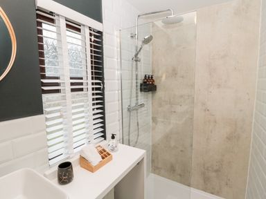 A bathroom with a shower area a white countertop with toiletries and a window with blinds at The Treeline in Swarland near Felton