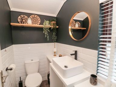 A bathroom with a white toilet and sink a round mirror wooden shelf with plants and decorative items at The Treeline Swarland near Felton