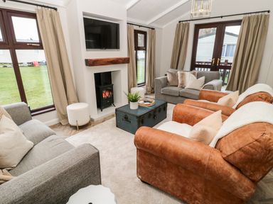 A living room with two gray sofas and two brown leather armchairs around a coffee table and a fireplace at The Treeline in Swarland near Felton