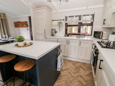 A kitchen with white cabinets a dark island with stools and a window above the sink at The Treeline in Swarland near Felton