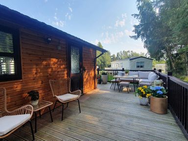 An outdoor wooden deck with chairs, table, potted plants, and a cabin at The Treeline in Swarland near Felton