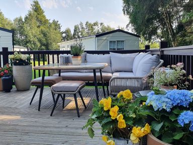An outdoor seating area with a table sofa stools and potted flowers on a wooden deck at The Treeline in Swarland near Felton