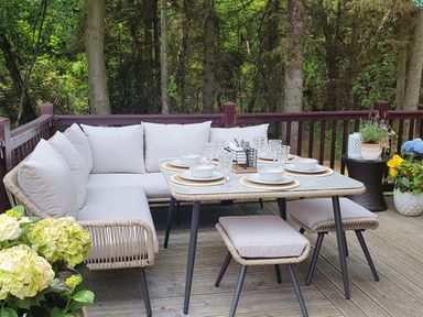 An outdoor dining area with a cushioned corner sofa table and stools surrounded by potted plants at The Treeline in Swarland near Felton