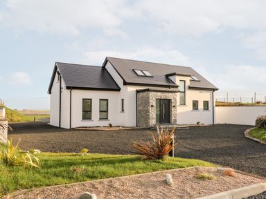 A modern house with white walls, black roof, and stone entrance surrounded by gravel driveway and plants at The Beachhouse in Meenlaragh near Gortahork, County Donegal