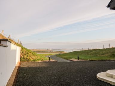 A gravel driveway leading to a grassy area with fences and water in the distance at The Beachhouse in Meenlaragh near Gortahork County Donegal