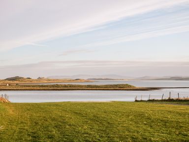 A grassy field leading to a body of water with hills in the background at The Beachhouse in Meenlaragh near Gortahork County Donegal