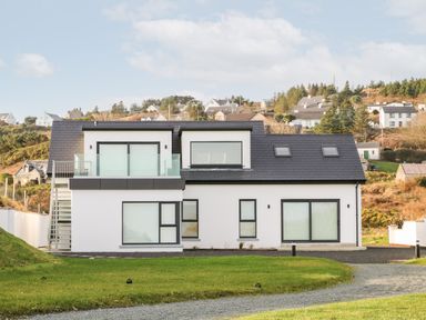 A modern two-story house with large windows and a glass balcony at The Beachhouse in Meenlaragh near Gortahork County Donegal