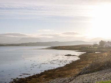 A coastal landscape with calm water a rocky shoreline grassy land and hills in the background at The Beachhouse in Meenlaragh near Gortahork County Donegal