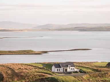 A house near a large body of water with hills in the background at The Beachhouse Meenlaragh near Gortahork County Donegal