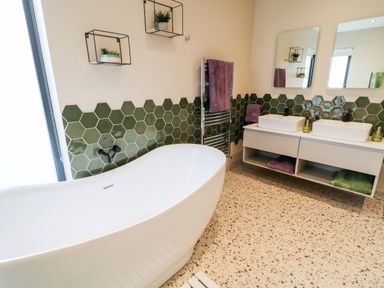A bathroom with a white freestanding bathtub green hexagonal wall tiles double sinks with mirrors and shelves with plants at The Beachhouse in Meenlaragh near Gortahork County Donegal