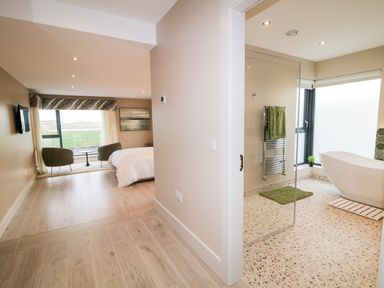 A bedroom with bed and chairs next to a bathroom with bathtub and towel rack at The Beachhouse in Meenlaragh near Gortahork County Donegal