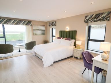 A bedroom with a bed two chairs a small table desk and lamps at The Beachhouse in Meenlaragh near Gortahork County Donegal