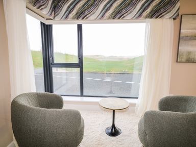 A sitting area with two gray armchairs and a small round table by a large window with white curtains at The Beachhouse in Meenlaragh near Gortahork County Donegal