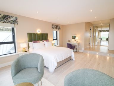A bedroom with a bed an armchair a dressing table and a mirrored wardrobe at The Beachhouse in Meenlaragh near Gortahork County Donegal