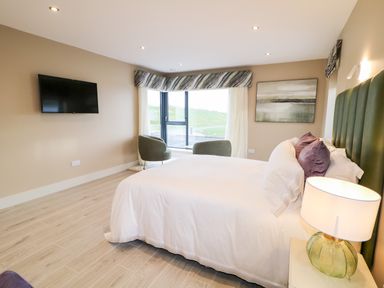 A bedroom with a bed bedside table lamp two chairs wall-mounted tv and a window at The Beachhouse in Meenlaragh near Gortahork County Donegal