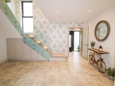 An entryway with stairs glass railing and a bicycle shaped table with a round mirror above at The Beachhouse in Meenlaragh near Gortahork County Donegal