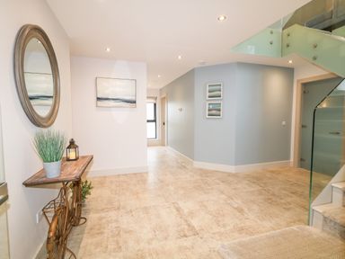 A hallway with a bicycle-shaped table holding a plant and lantern a round wall mirror paintings on walls and glass staircase railing at The Beachhouse in Meenlaragh near Gortahork County Donegal