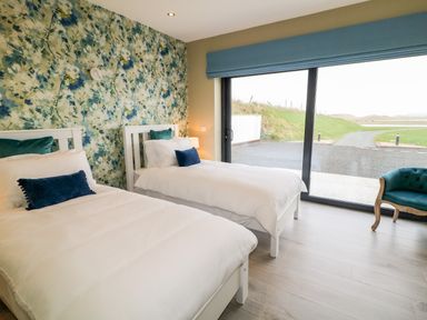 A bedroom with two single beds white bedding floral wallpaper a blue chair and sliding glass doors at The Beachhouse in Meenlaragh near Gortahork County Donegal