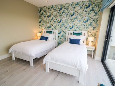 A bedroom with two single beds with white linens and blue cushions against a floral wallpaper at The Beachhouse in Meenlaragh near Gortahork County Donegal