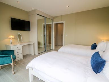 A bedroom with two beds a desk with a lamp and mirror a wall-mounted tv and a teal chair at The Beachhouse in Meenlaragh near Gortahork County Donegal
