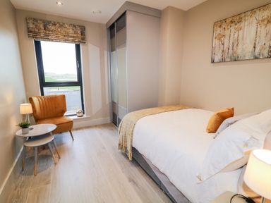 A bedroom with a bed a bedside table with a lamp two nested tables an armchair a window and a wardrobe at The Beachhouse in Meenlaragh near Gortahork County Donegal